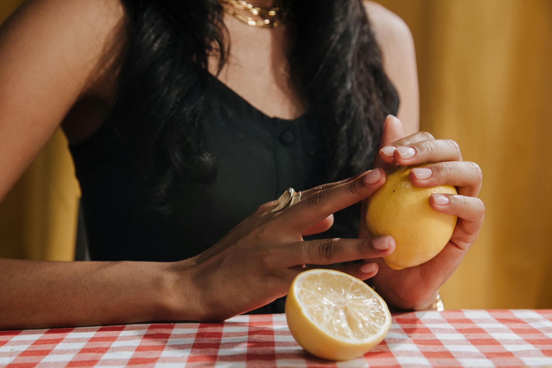 Close-up of a woman holding a fresh lemon at a dining table, symbolizing natural sensation and refreshed awareness.