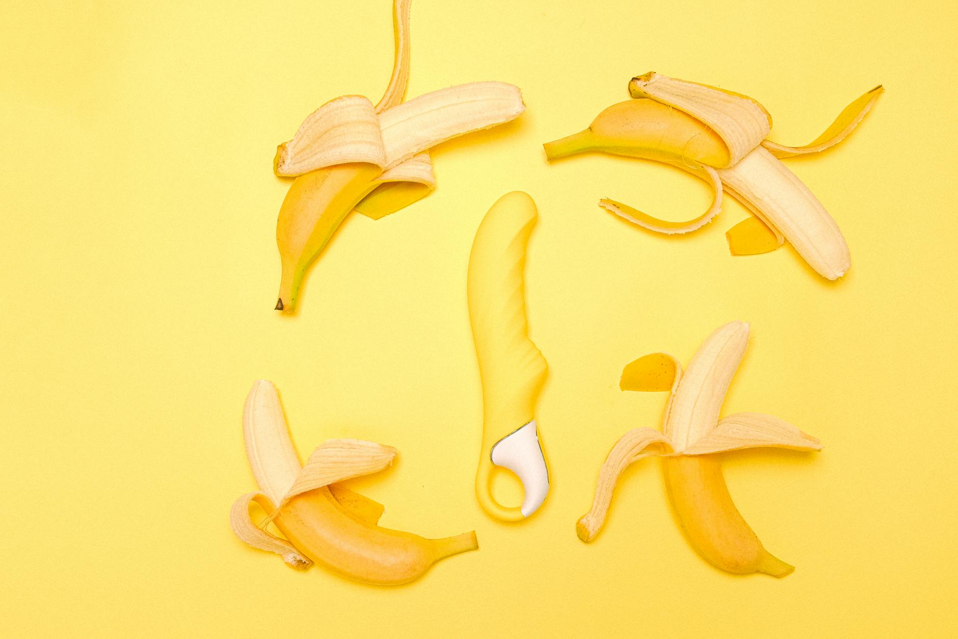 Yellow lemon vibrator surrounded by fresh lemons on a bright yellow background, symbolizing pleasure and natural sensation