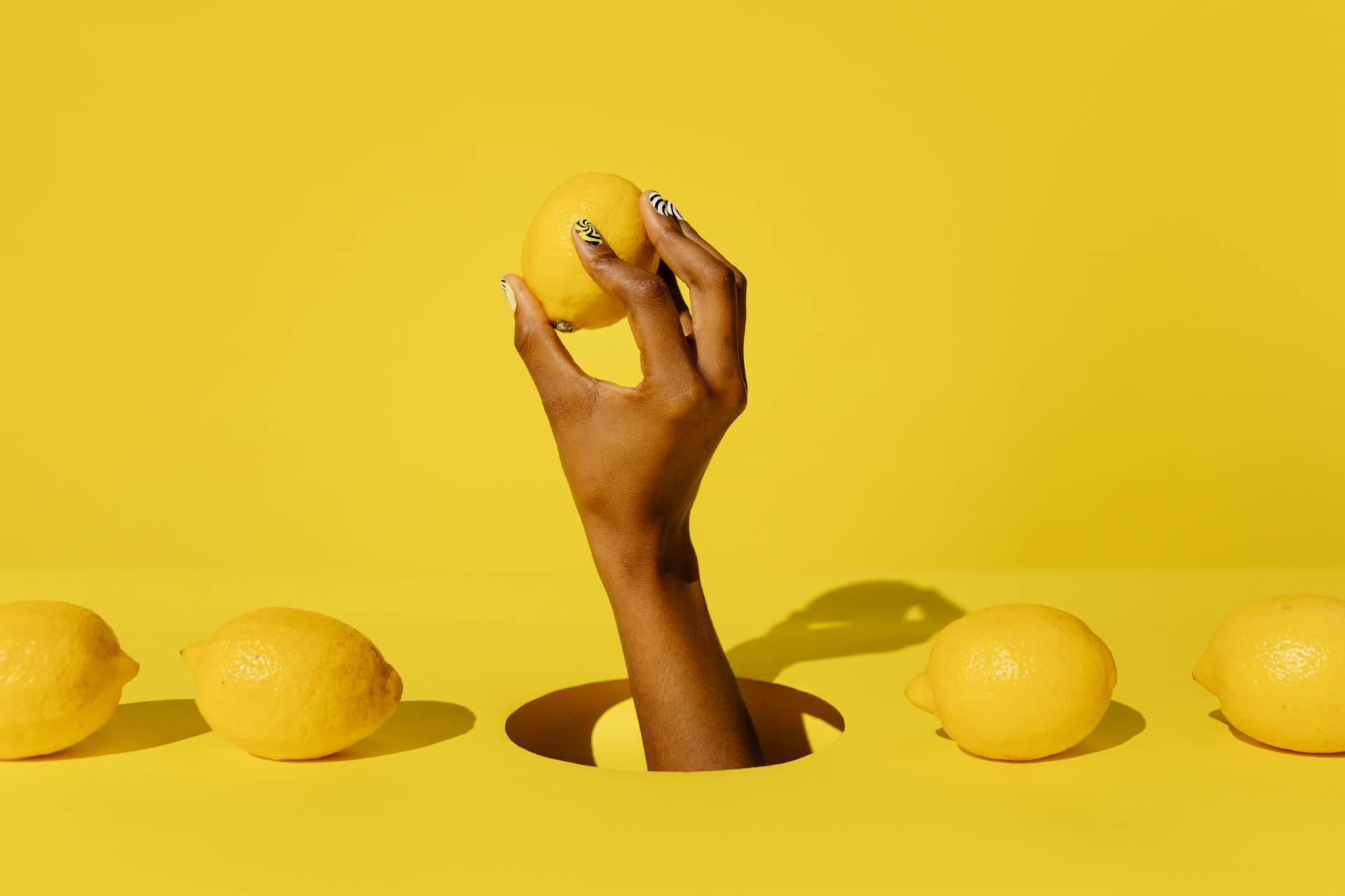 A hand holding a fresh lemon against a vivid yellow background, symbolizing renewal and reconnection to simple pleasure.